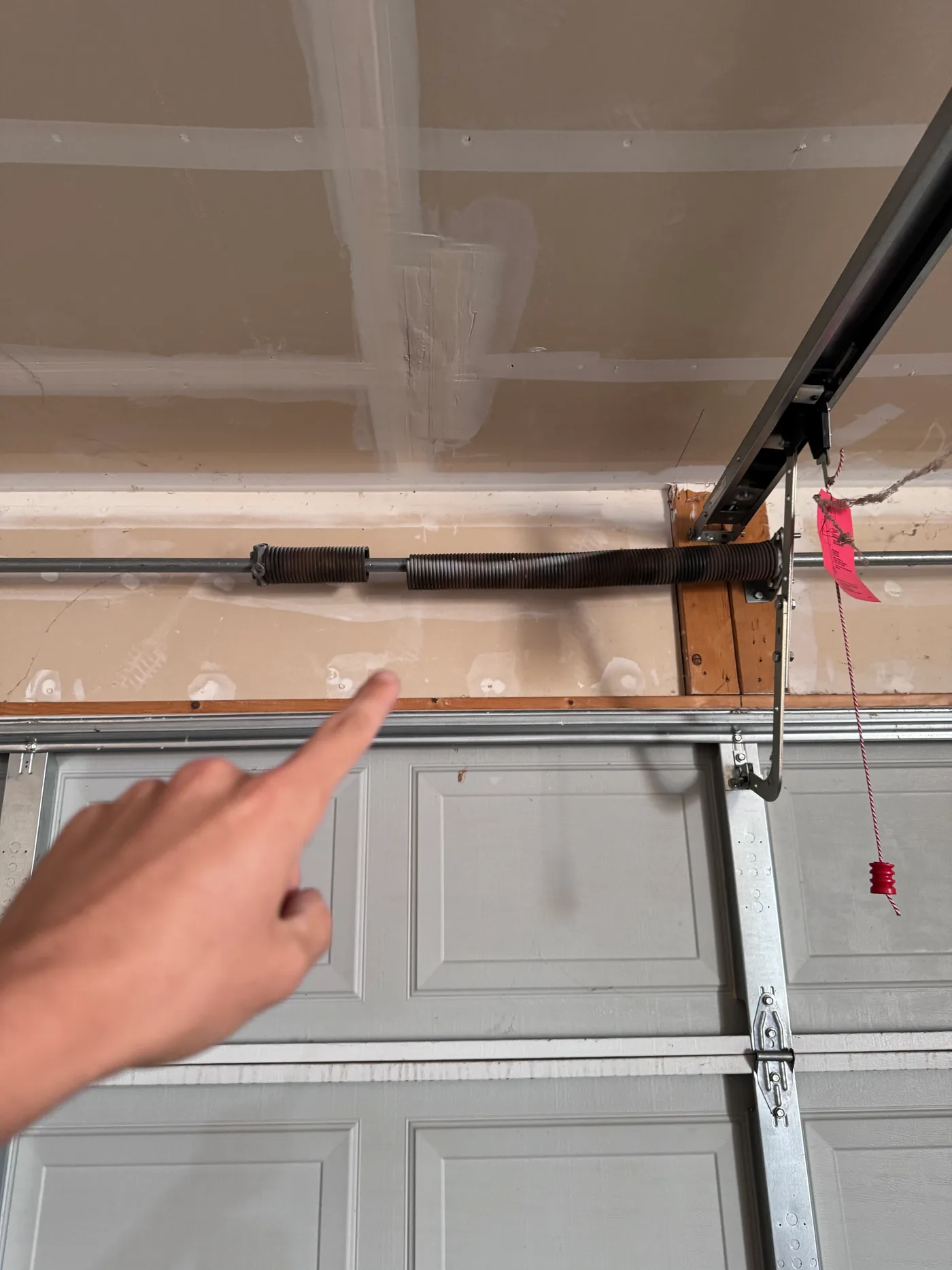 A person points toward a visible gap in a broken garage door torsion spring