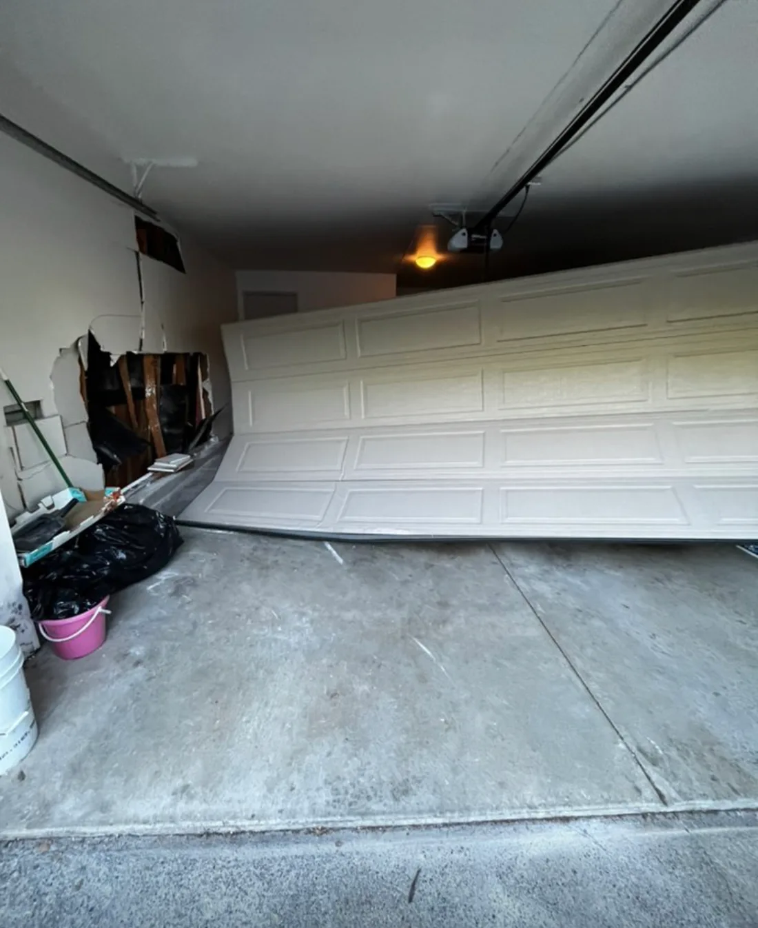 A severely damaged garage door sitting unevenly inside a garage