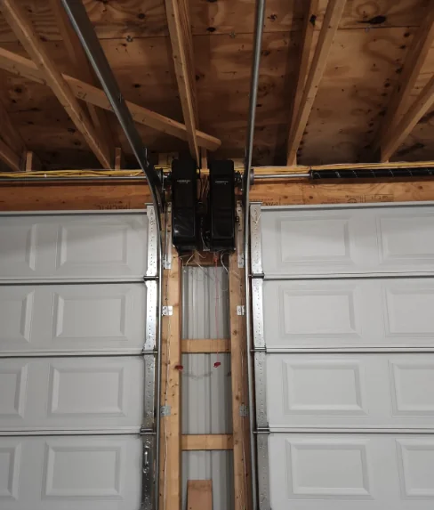 Two Chamberlain side-mount openers installed between two garage doors beneath exposed ceiling framing