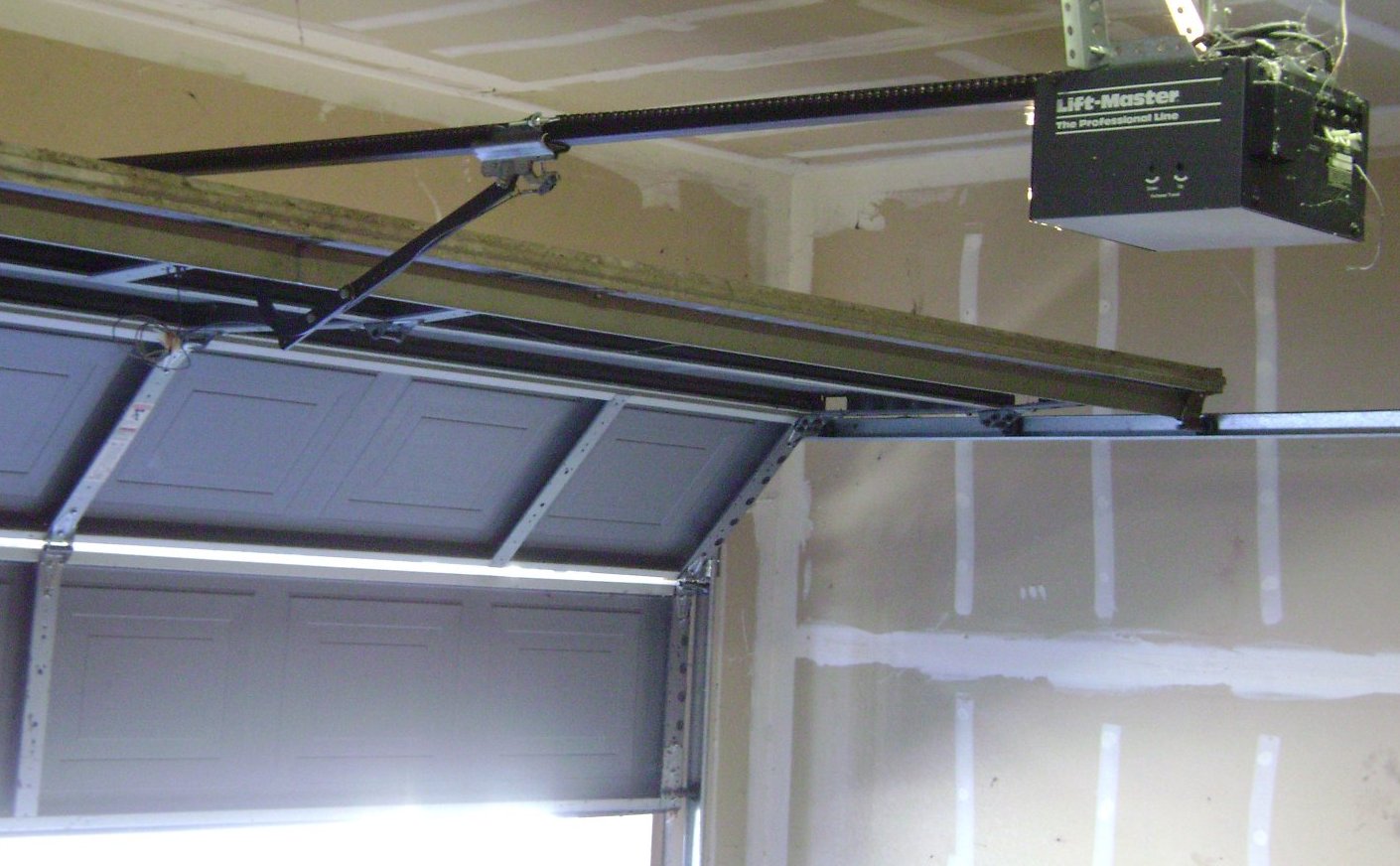 Real photograph of an older ceiling-mounted chain-drive LiftMaster opener and its rail inside a garage.